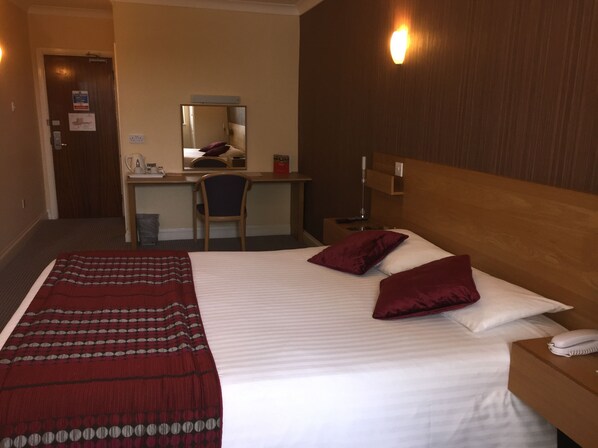 A hotel room with a bed, a desk, a chair, a nightstand, and a phone.