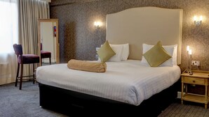 Ett hotellrum med en stor säng, en stol, ett nattduksbord och en spegel.