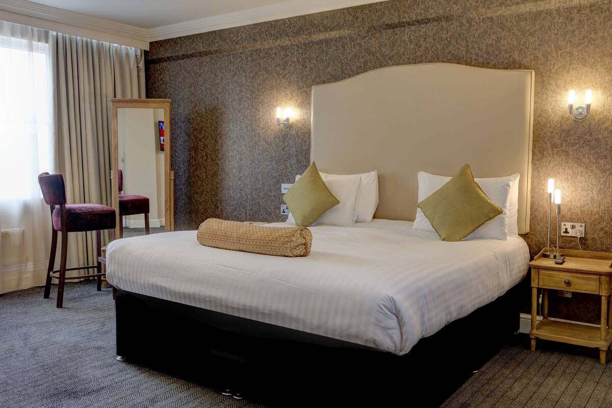 A hotel room with a large bed, a chair, a nightstand, and a mirror.