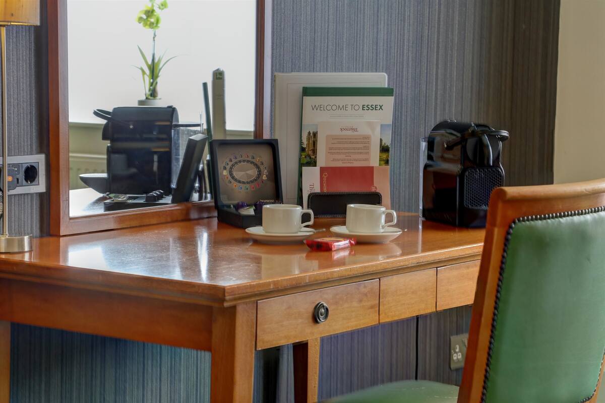 A hotel reception desk with a coffee maker, two cups, a welcome sign, and a plant.