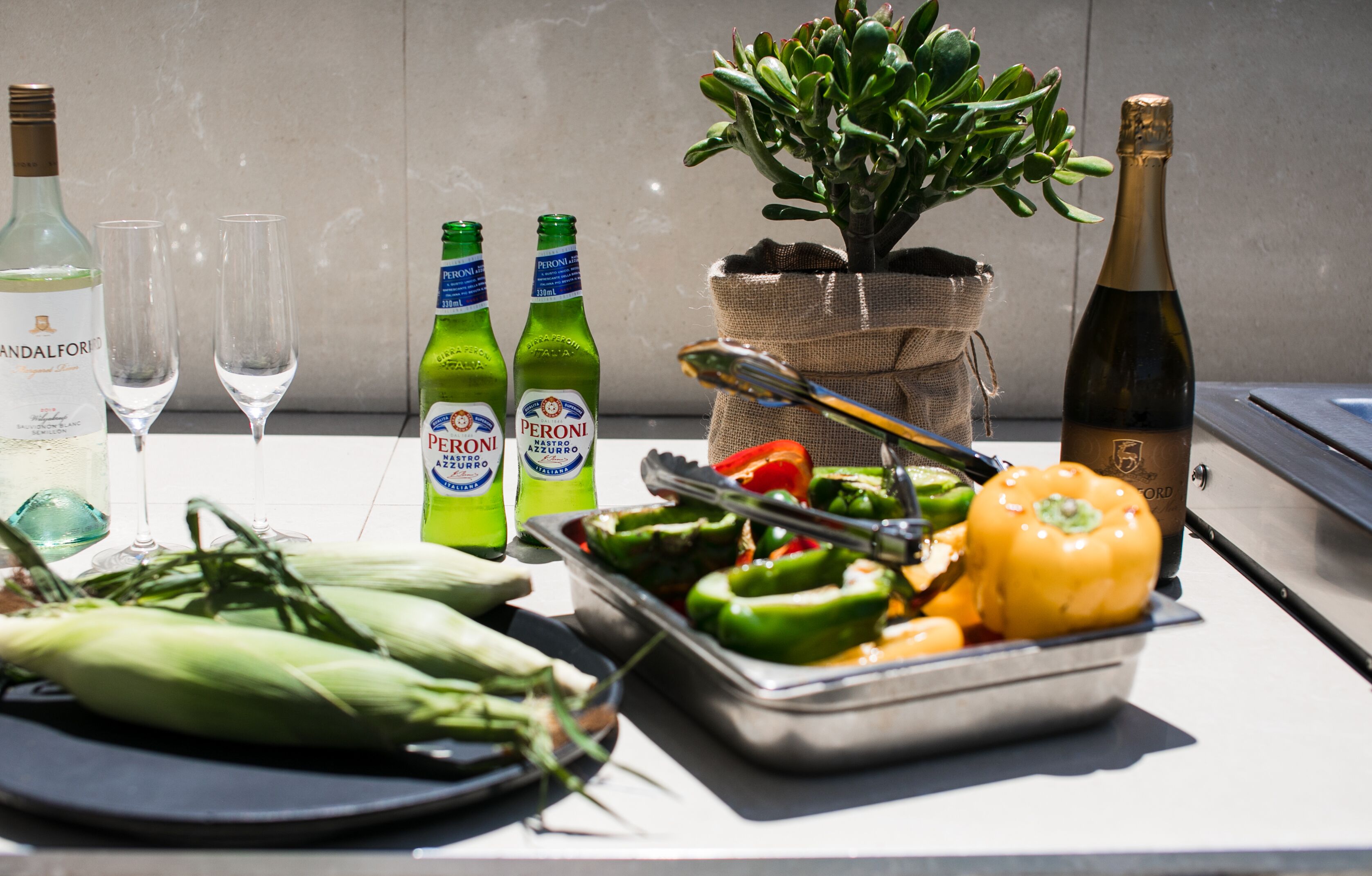 Ein Tisch mit Peroni-Flaschen, einer Weinflasche und einer Pflanze in einem Jutbeutel.