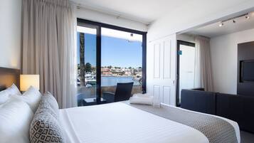 A hotel room with a large bed, a sofa, a TV, and a view of a marina.
