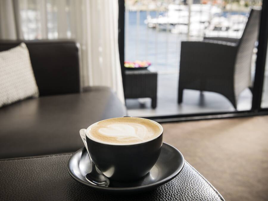 Una taza de café sobre un platito, sobre una mesa, con vistas a un balcón y una zona de estar al aire libre.