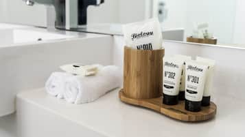 A bathroom with a wooden tissue holder, two bottles of shampoo, and a rolled towel on a white countertop.