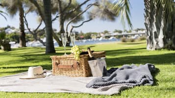 Un'area erbosa con un picnic: un cesto in vimini contiene una bottiglia, bicchieri e grappoli d'uva, una coperta e un cappello.