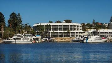 A marina with multiple boats docked, a large white building with balconies, and surrounding greenery.