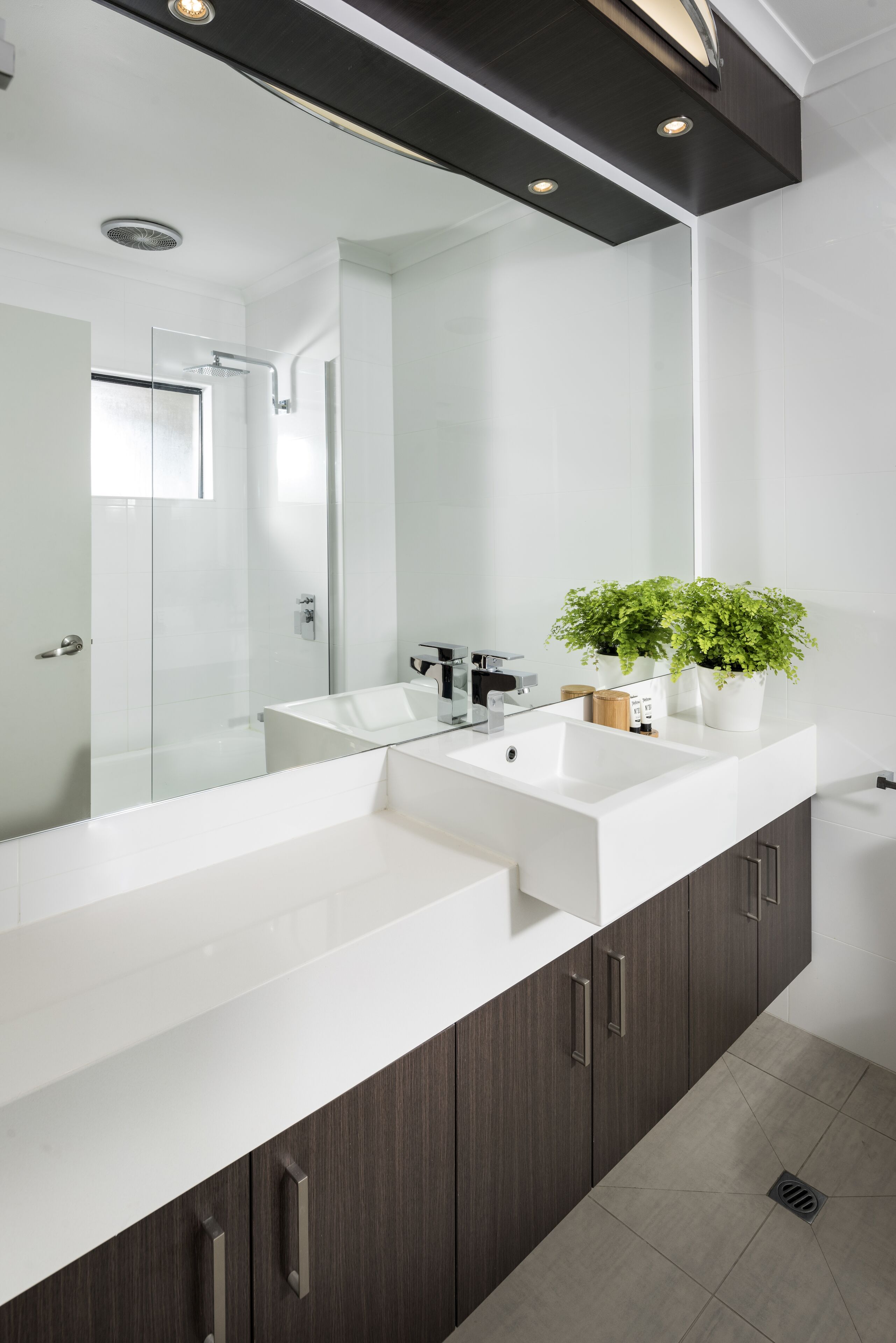 A modern bathroom with a large mirror, two sinks, dark wood cabinets, and a potted plant.