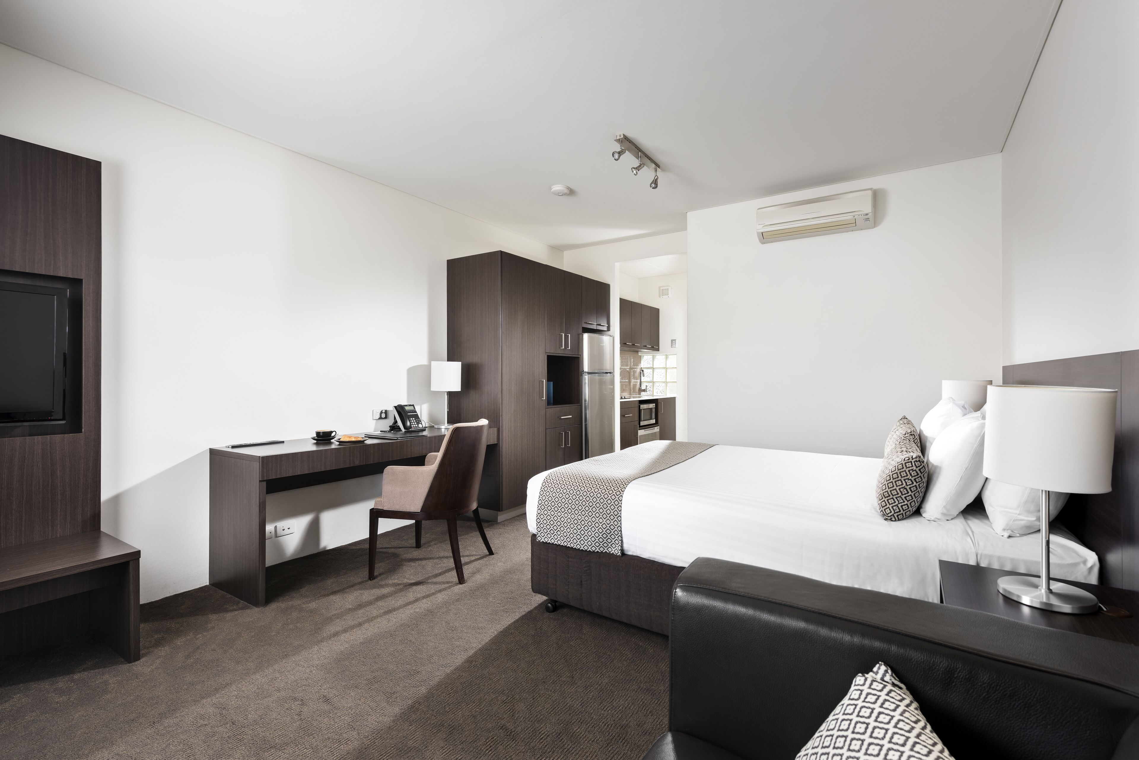 Una habitación de hotel moderna con cama, escritorio, silla y kitchenette.