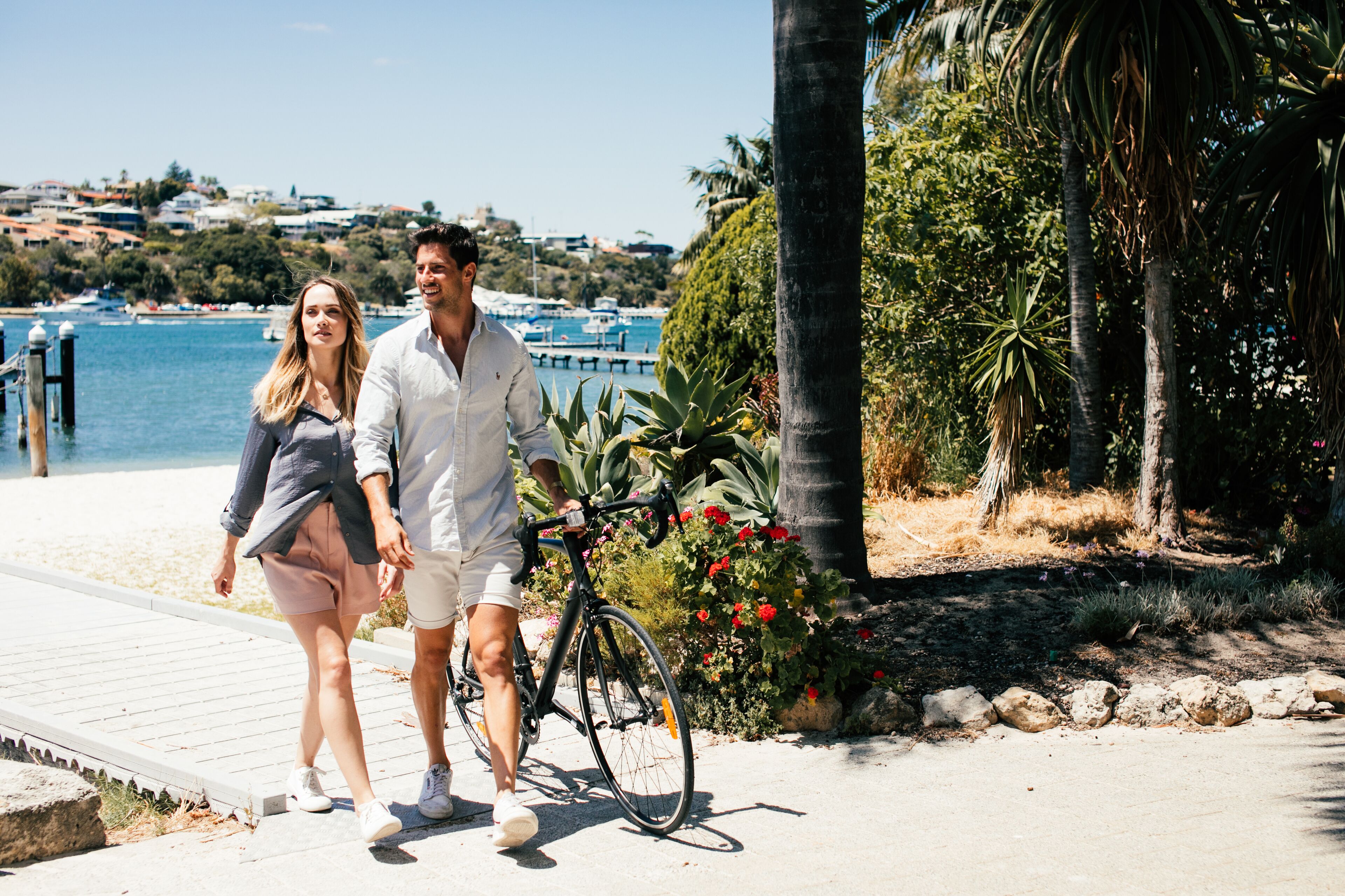 Un couple se promène le long d’une promenade en bord de mer, avec un vélo et un sentier pavé de pierres.