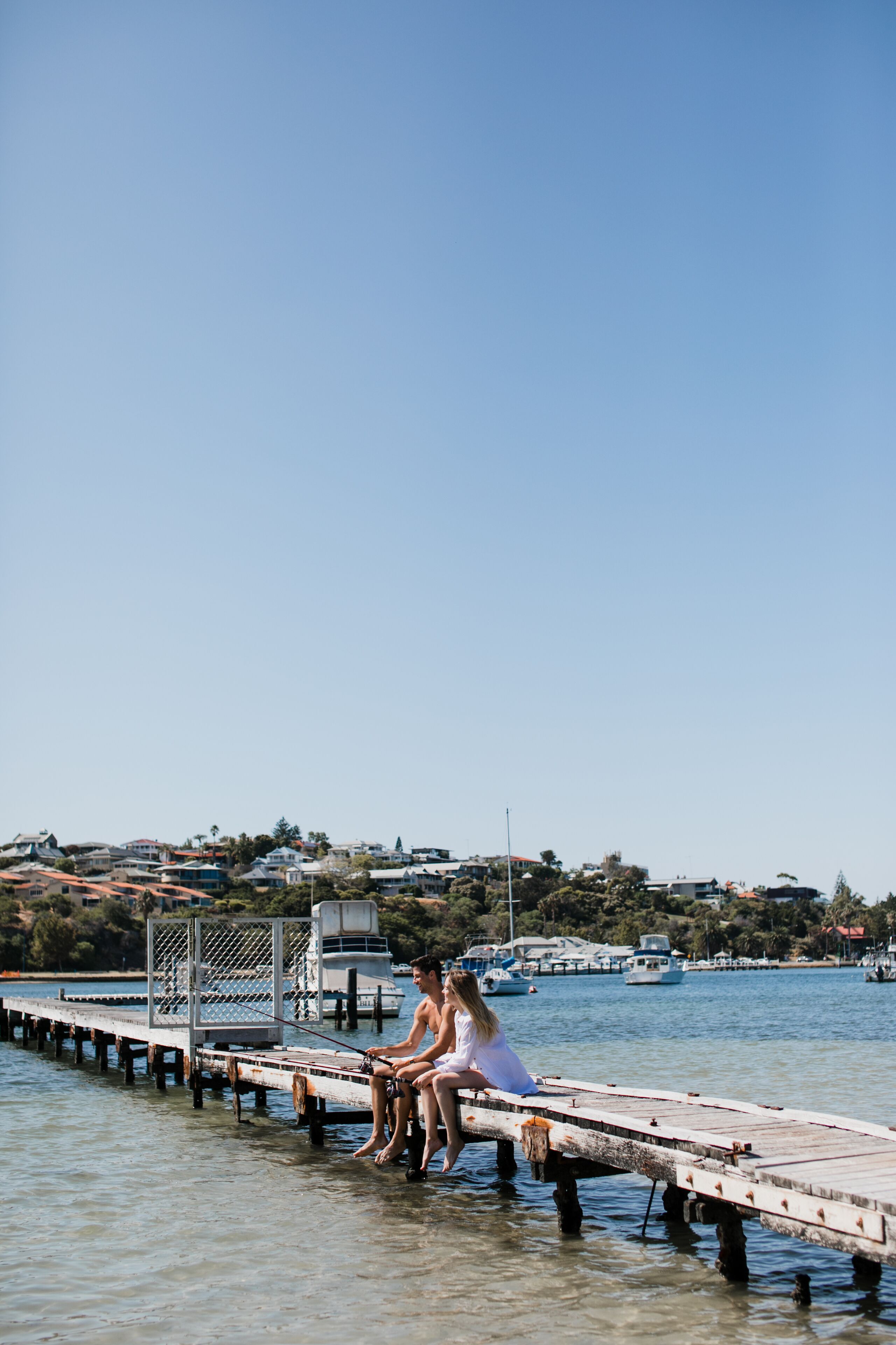 Un muelle se adentra en aguas tranquilas, con dos personas sentadas al final.