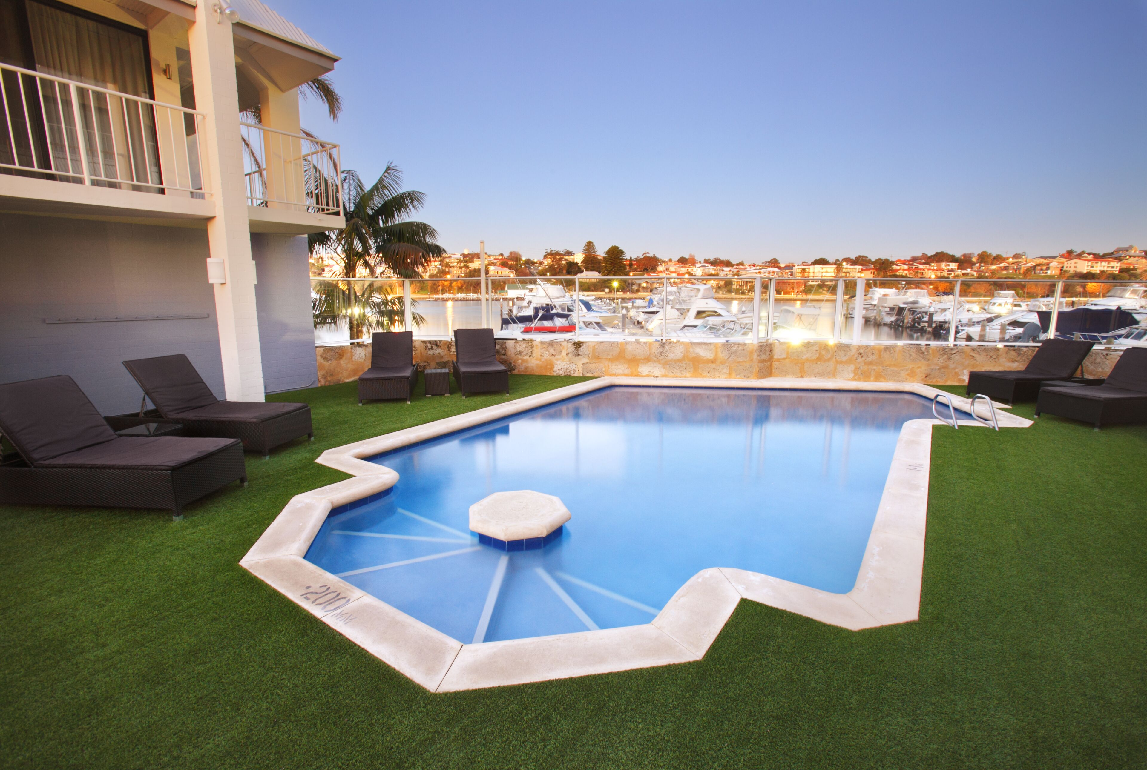A swimming pool with a view of boats and a building with a balcony.