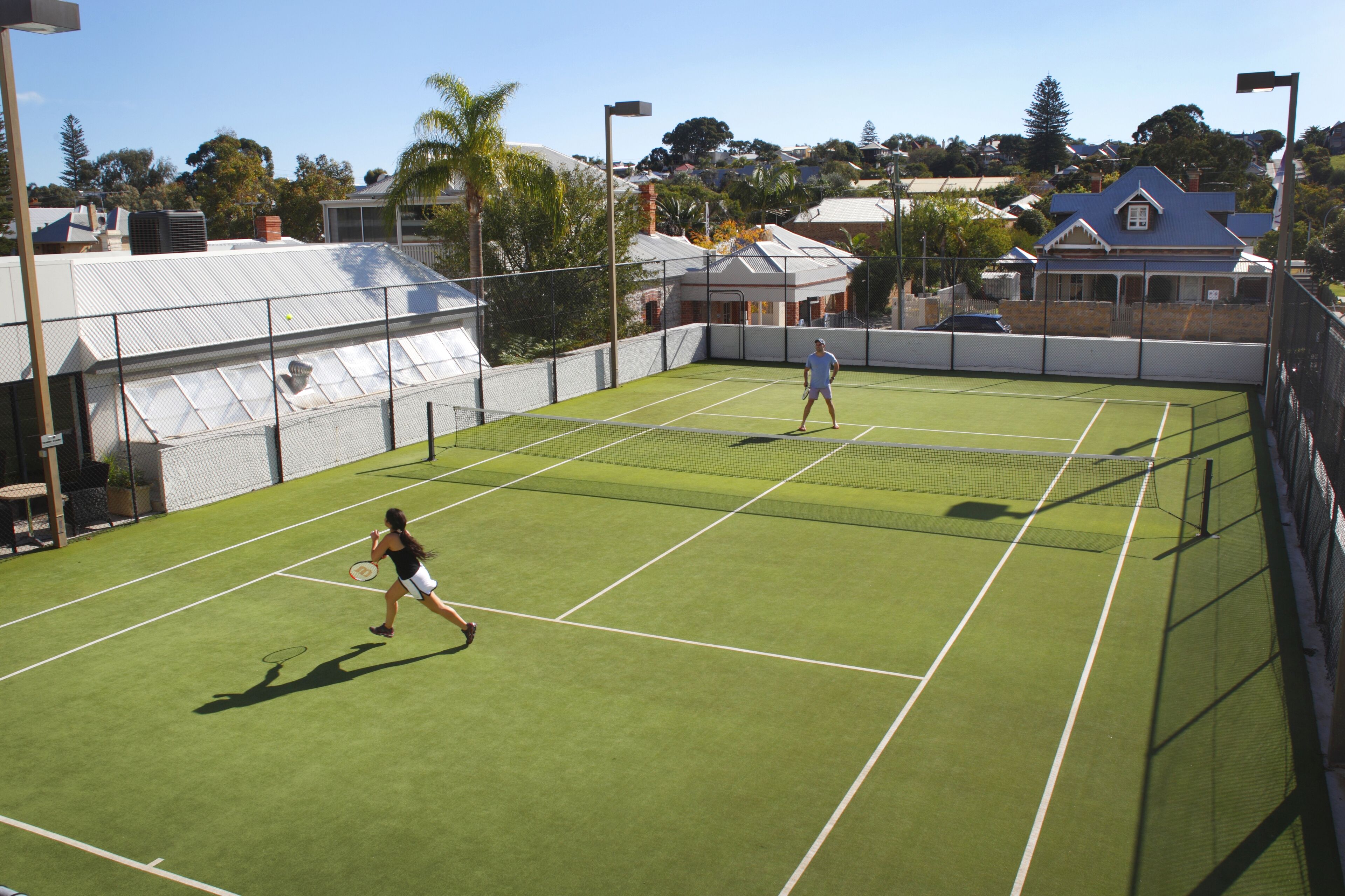 A tennis court with two players, surrounded by a fence and trees.