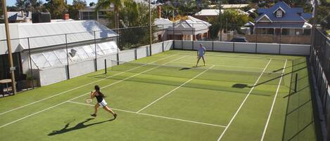 A tennis court with two players, surrounded by a fence and trees.