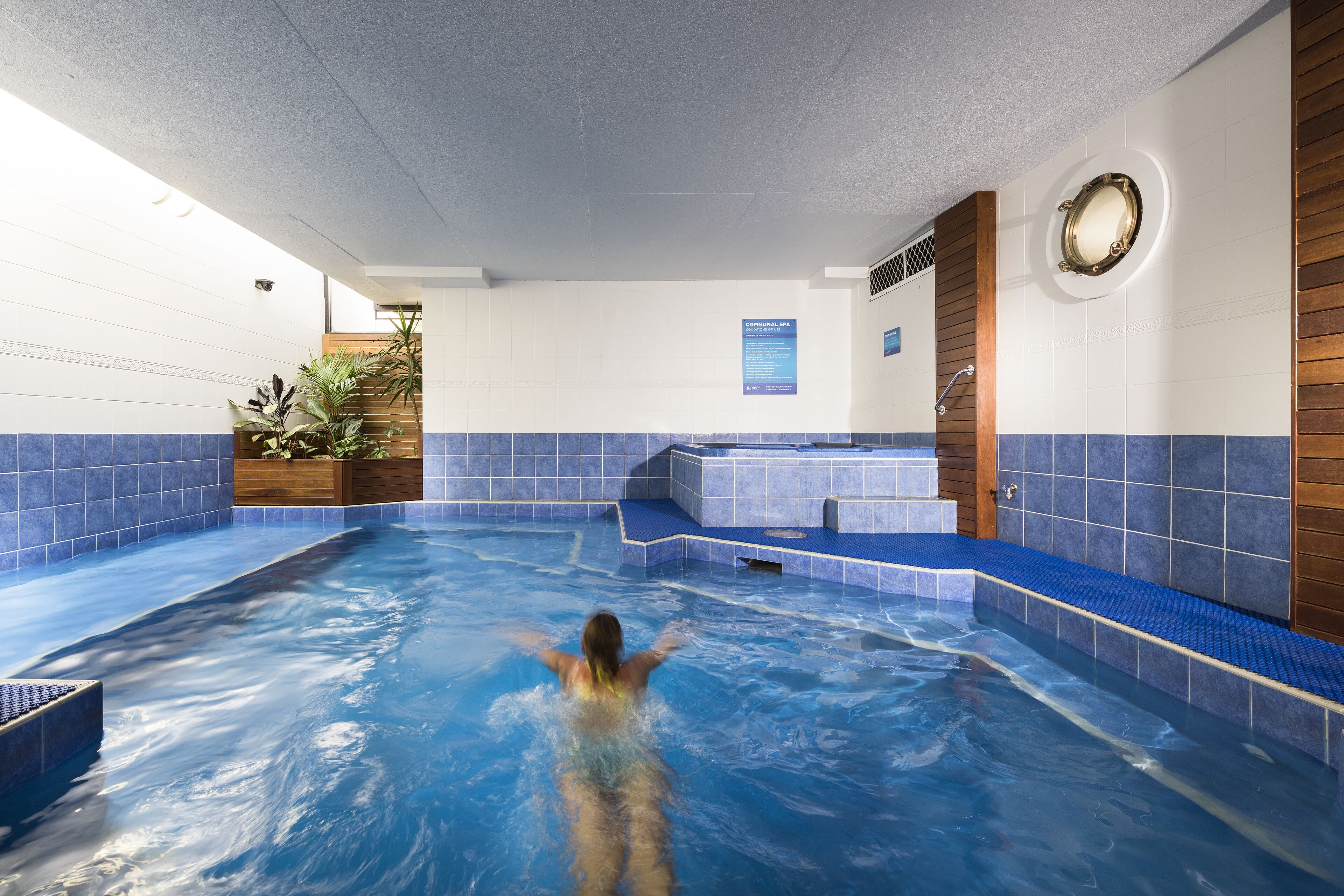 Ein Schwimmbecken mit einer Person, gefliesten Wänden und einer Holzbank.