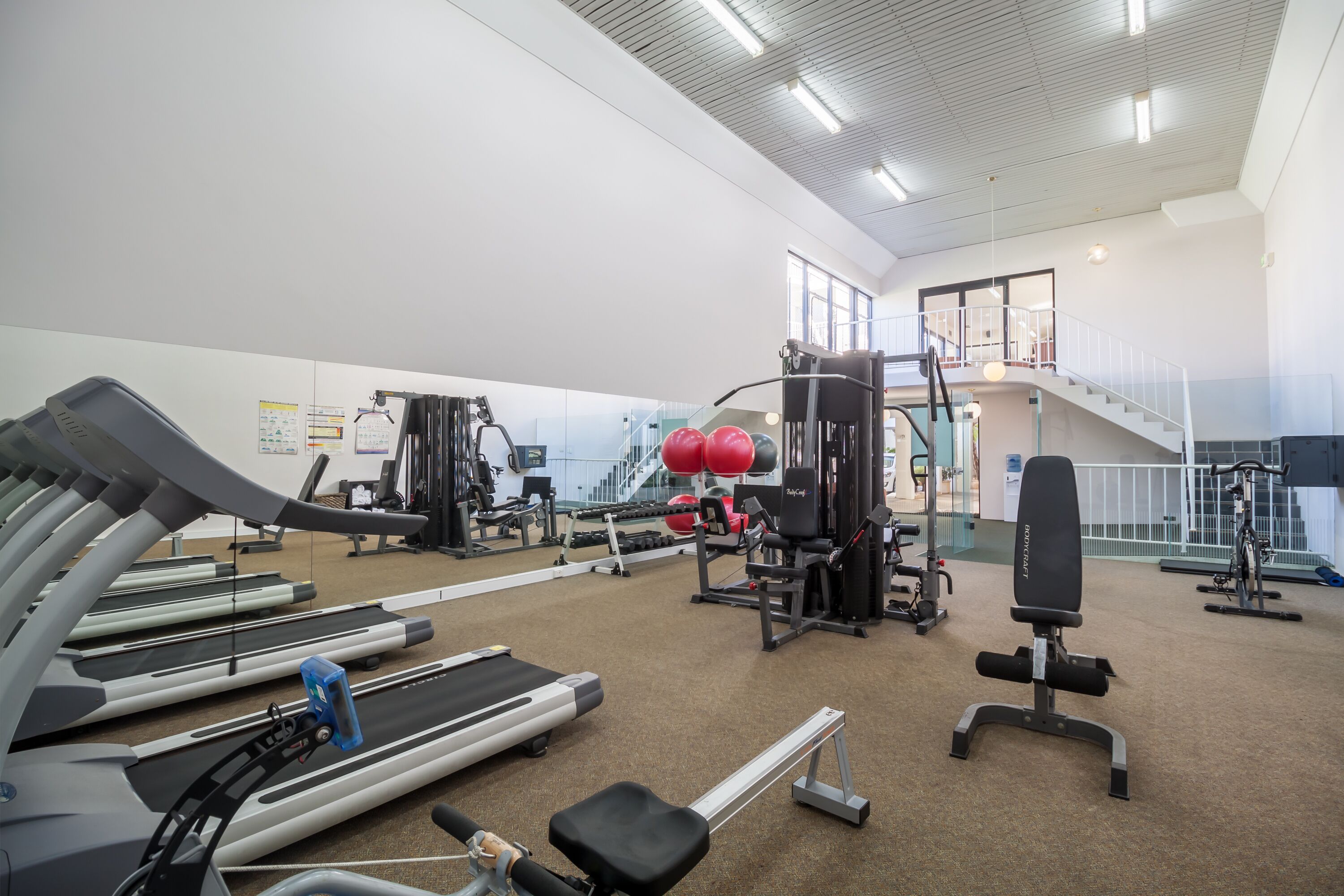 Una palestra con tapis roulant, macchinari per pesi e una scala.
