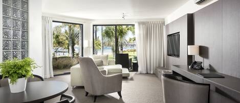 A modern hotel room with a large window, a flat-screen TV, a desk, and a comfortable seating area.