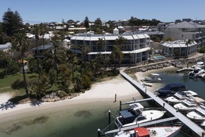A marina with boats docked, a sandy beach, and a building with a curved roof.