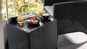 Fletstol og bord med morgenmadsprodukter på en balkon med udsigt over en lysthavn med både og palmer.