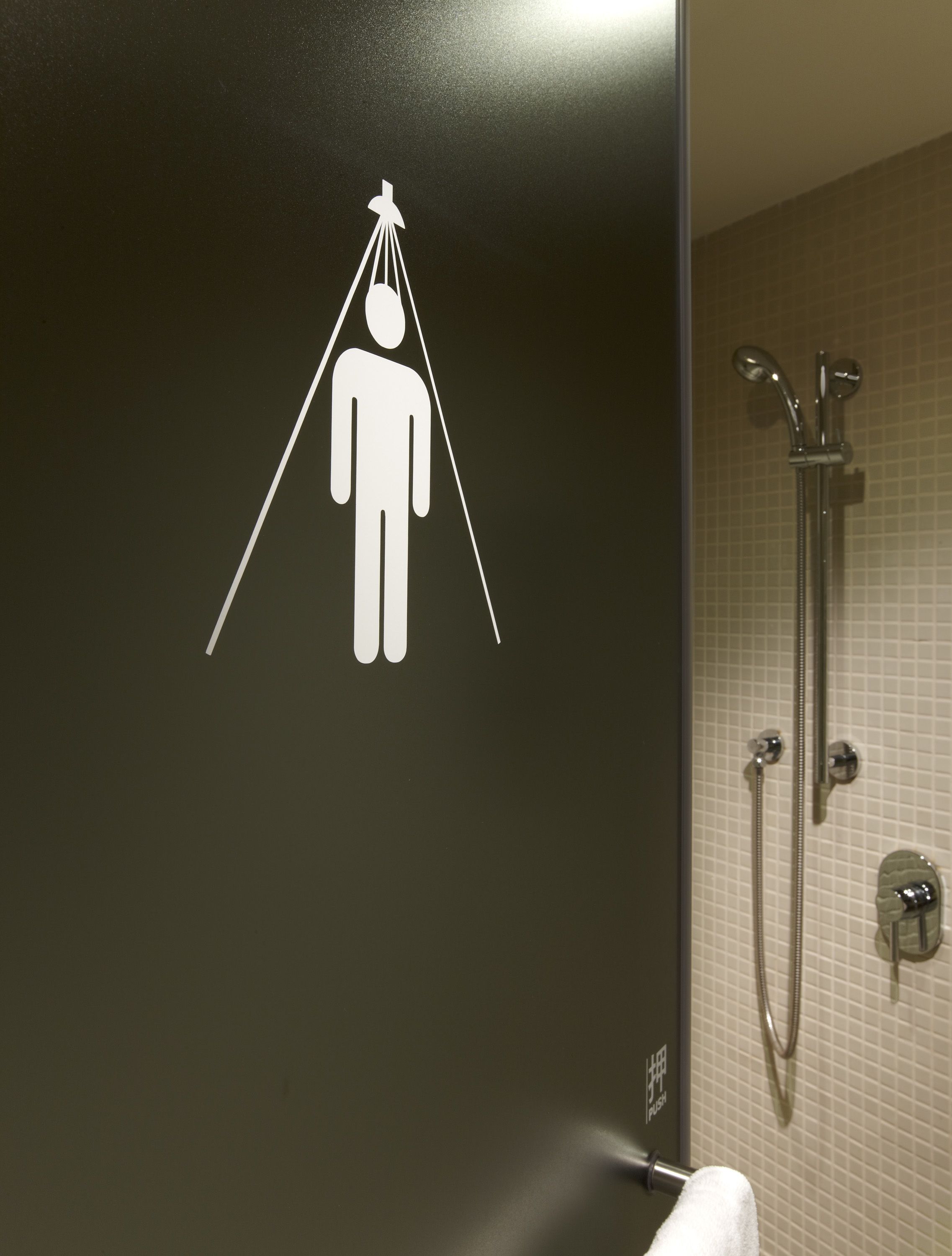 A bathroom with a shower, a towel rack, and a sign indicating the location of the toilet.