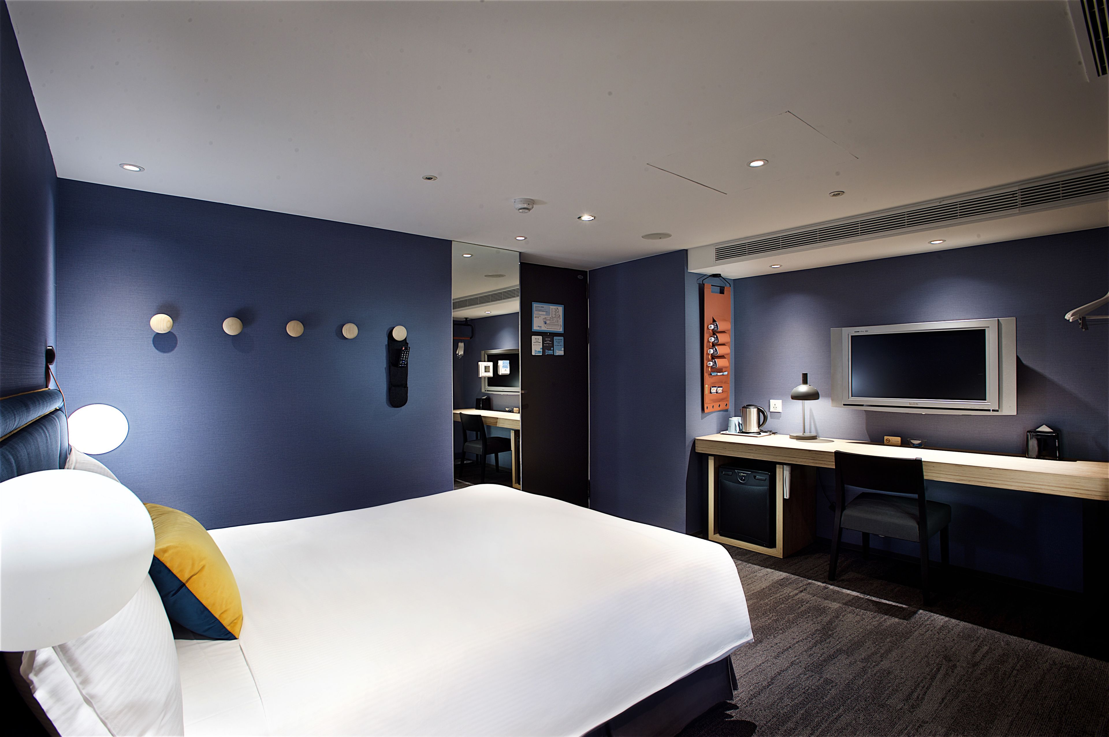 A modern hotel room with a large bed, a desk, a flat-screen TV, and a mirror.