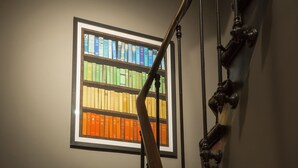 A staircase with a wooden handrail and a framed book collection on the wall. - Monsieur Helder (Paris)