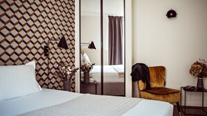 A hotel room with a bed, a chair, a nightstand, a lamp, a mirror, and a patterned wall. - Monsieur Helder (Paris)