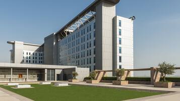 A modern hotel with a curved facade, multiple floors, and a well-maintained lawn area.