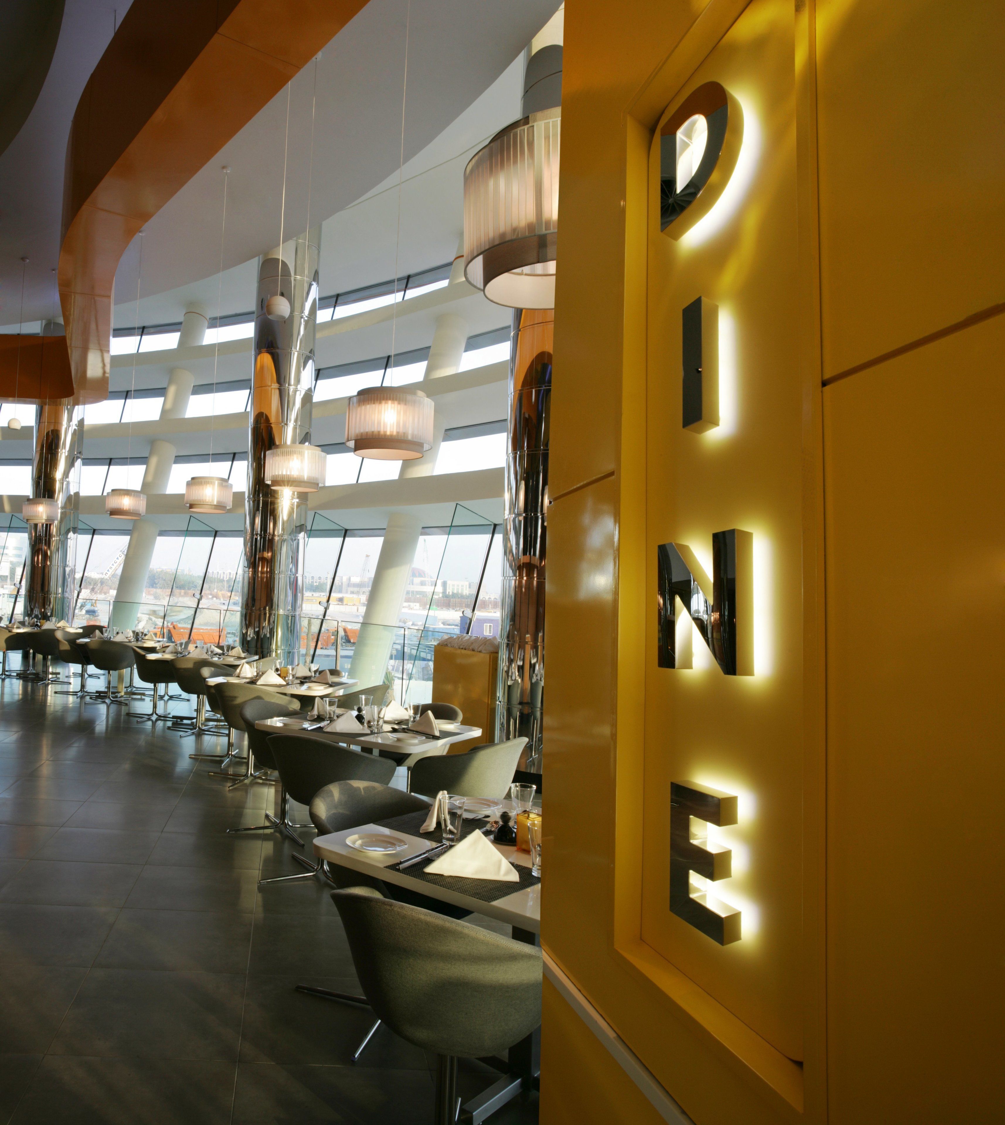 Un espace repas moderne, doté de tables et de chaises, de grandes fenêtres et d’une enseigne lumineuse bien visible sur le mur.