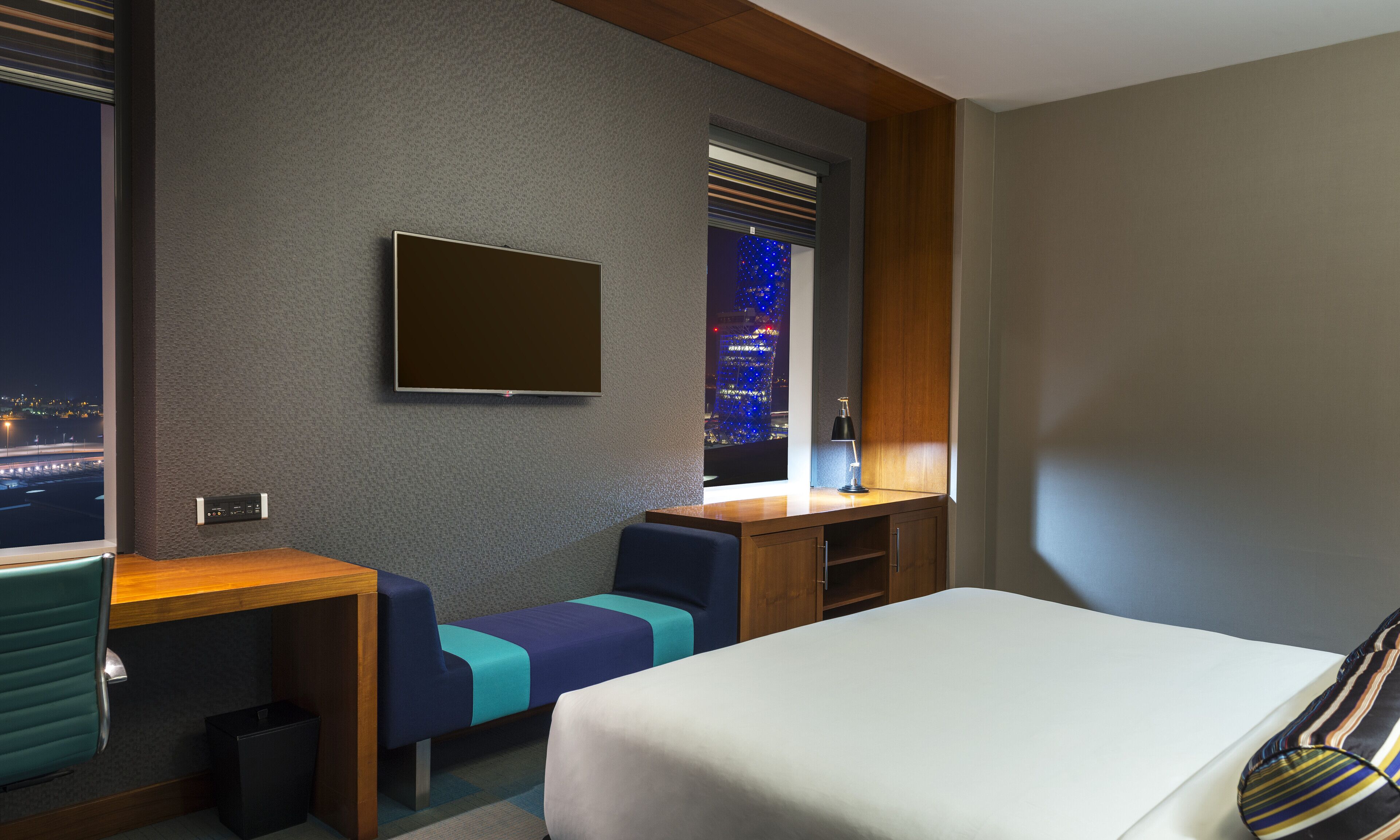 A hotel room with a bed, a desk, a chair, and a TV mounted on the wall.