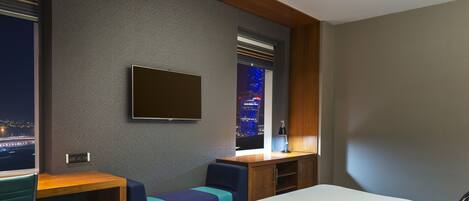 A hotel room with a bed, a desk, a chair, and a TV mounted on the wall.
