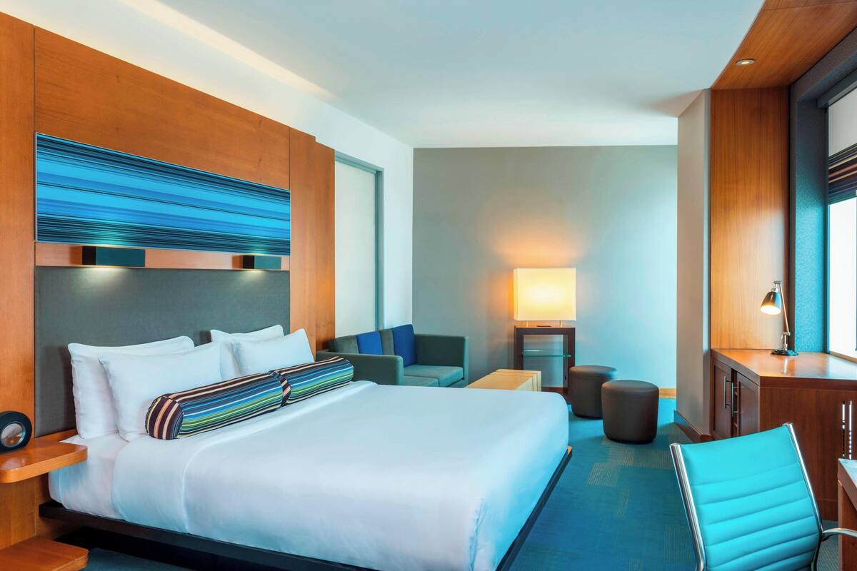 A modern hotel room with a large bed, a desk, a chair, and a sofa.