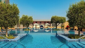A swimming pool with tiled edges, surrounded by lounge chairs and trees. - Aloft by Marriott Abu Dhabi (Abu Dhabi)