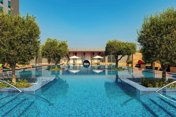 A swimming pool with tiled edges, surrounded by lounge chairs and trees.