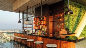 A bar with a wooden counter, multiple stools, and a green wall. - Aloft by Marriott Abu Dhabi (Abu Dhabi)