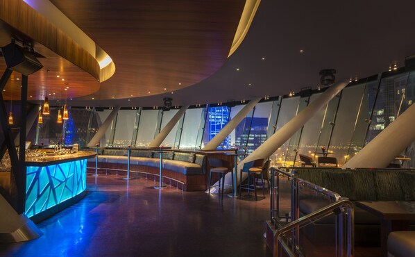 A modern interior with a bar area, seating, and large windows offering city views. - Aloft by Marriott Abu Dhabi (Abu Dhabi)