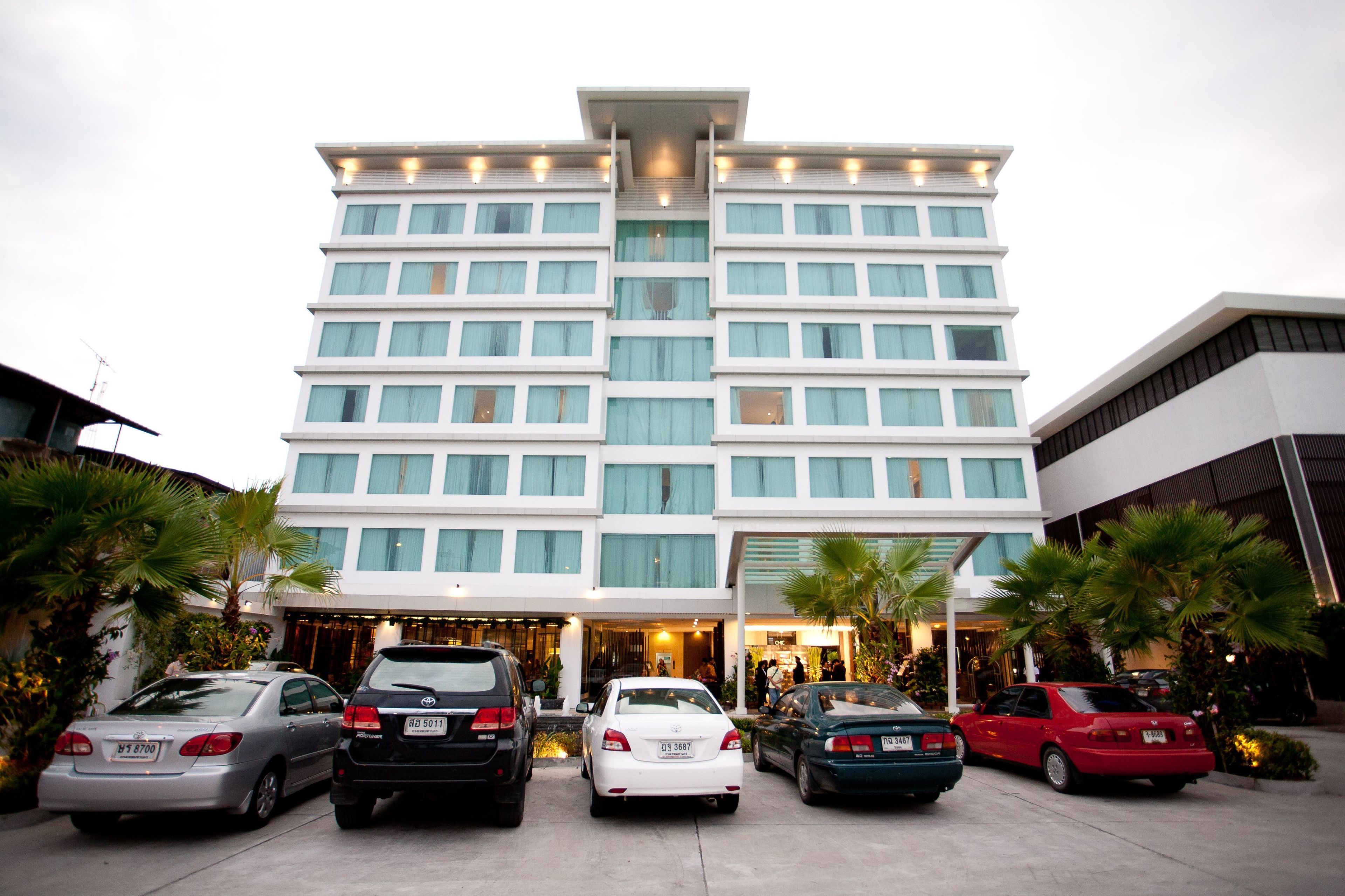 A multi-story hotel with a modern design, featuring a central entrance and a parking area with several cars.