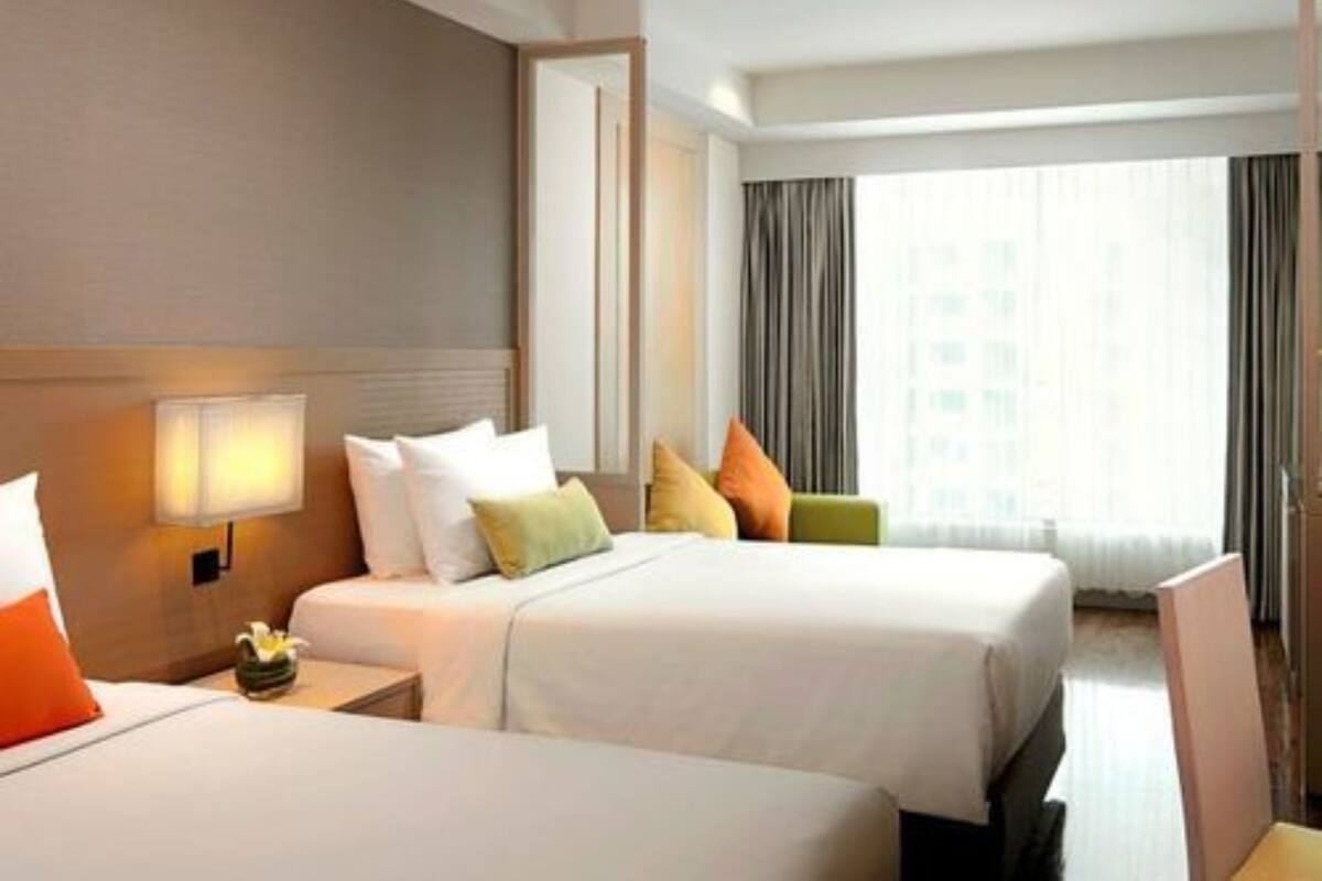 A hotel room with two beds, a nightstand, a lamp, and a window with curtains.