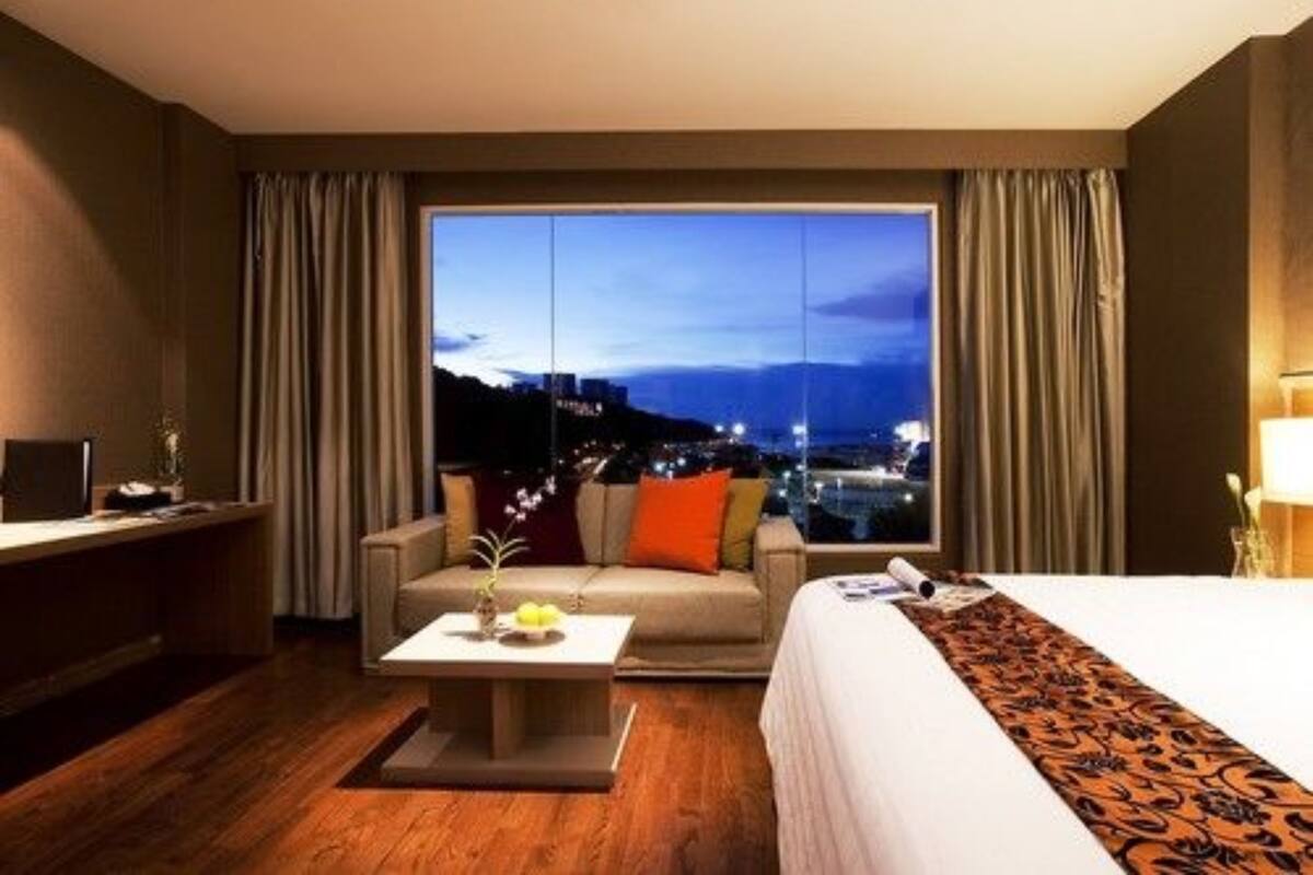 A hotel room with a large window, a bed, a sofa, a coffee table, and a desk.