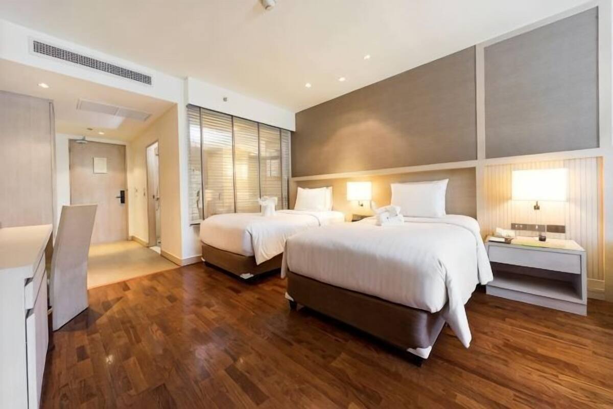 A hotel room with two beds, a desk, and a bedside table with lamps.