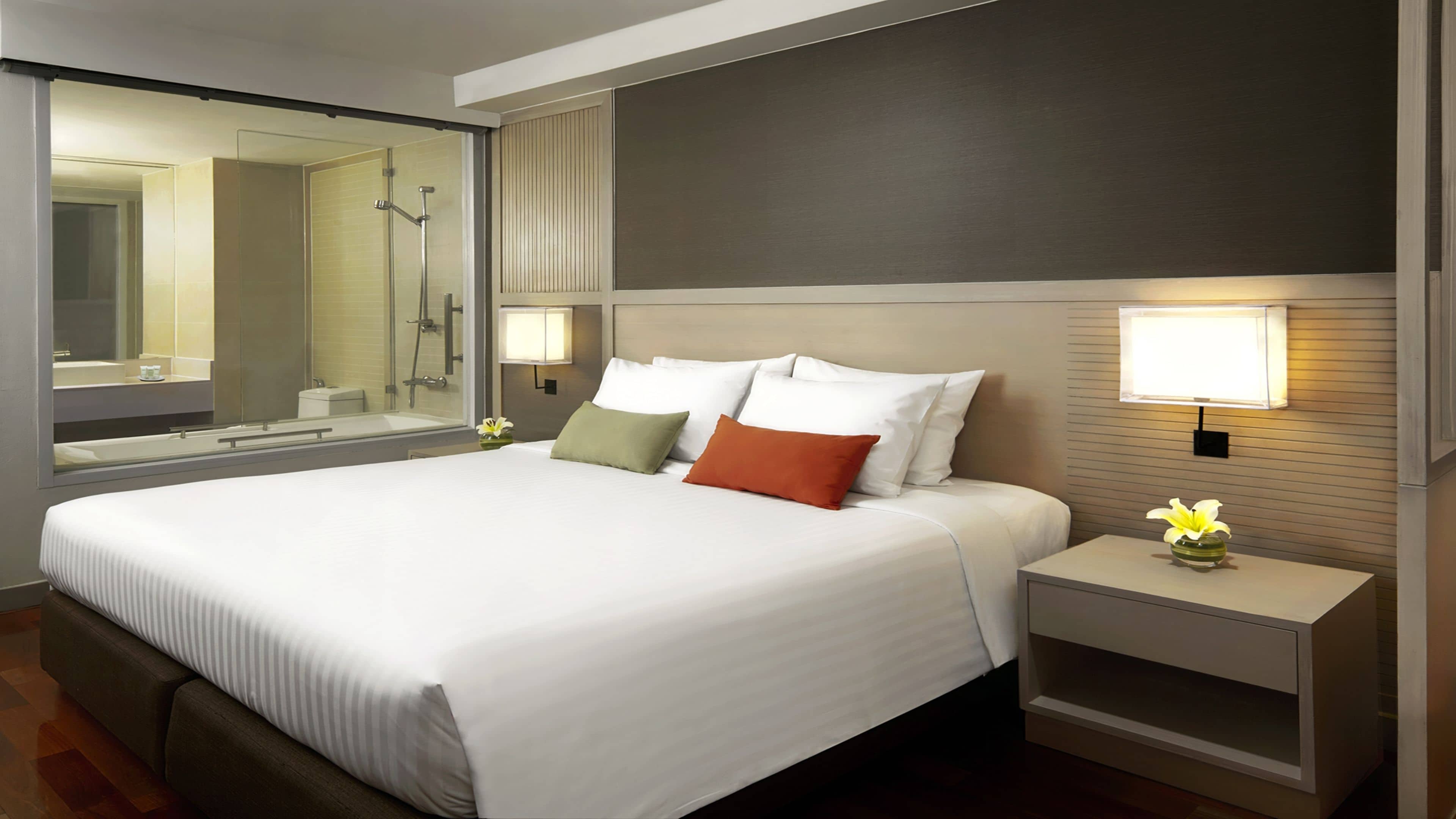 Une chambre d’hôtel avec un grand lit, une table de chevet avec une lampe, un miroir et un espace douche.