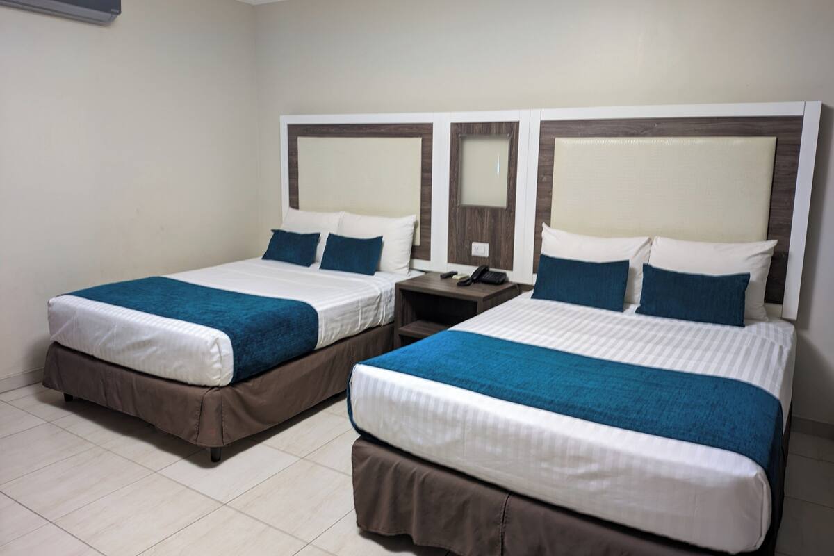 A hotel room with two beds, each with a blue and white bedspread, a wooden headboard, and a nightstand with a phone and lamp.