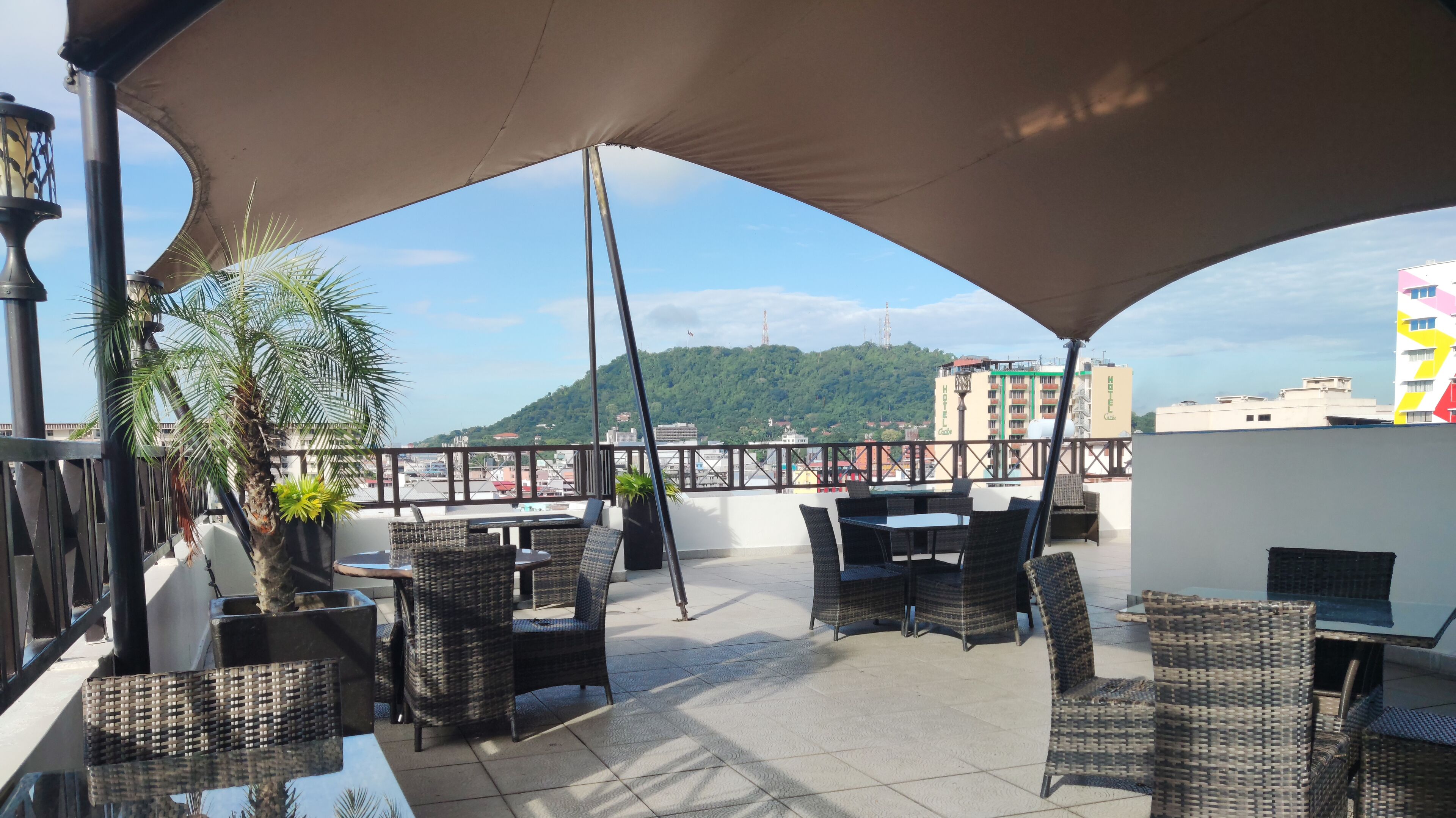 Terraço no telhado com móveis de vime, uma grande cobertura e vista para a cidade e colinas.