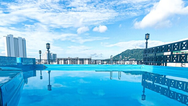 Una piscina en la azotea con agua azul cristalina, rodeada de edificios modernos y un puente.