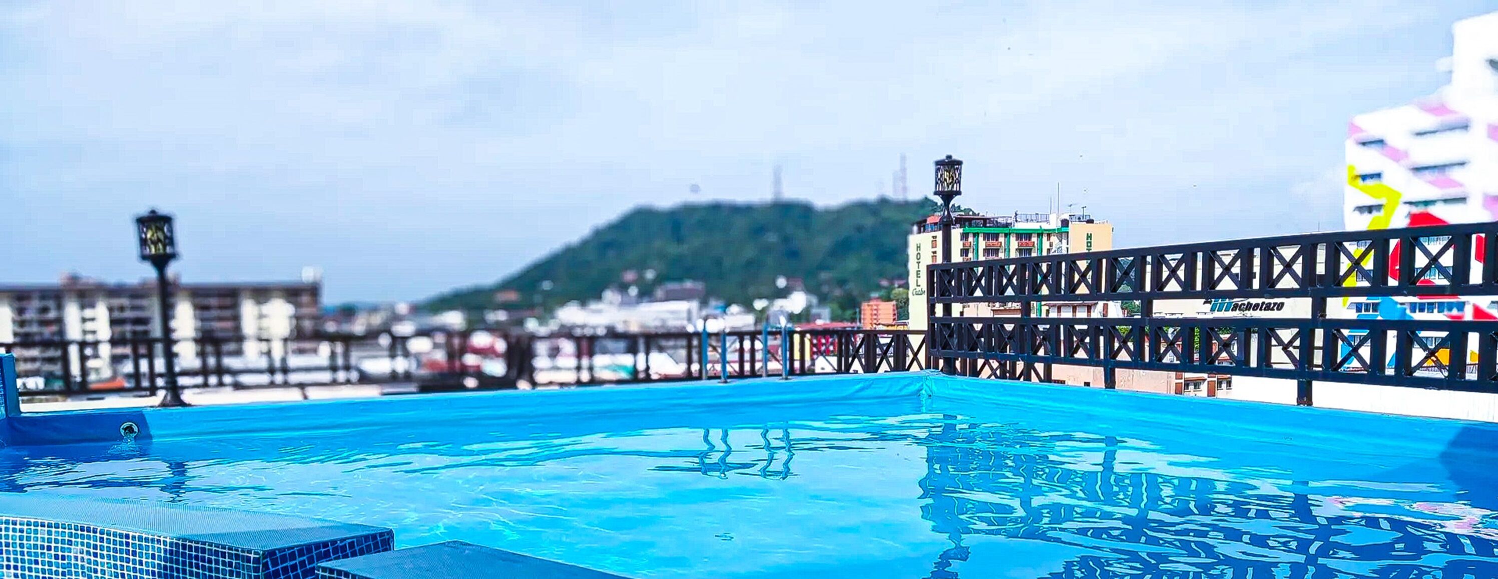 Una piscina en la azotea con vistas a un paisaje urbano y una colina al fondo.