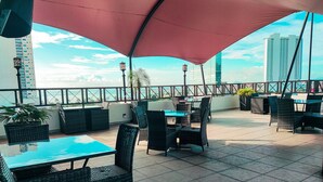 Un patio al aire libre con mesas y sillas, un toldo rojo y vistas del horizonte urbano.