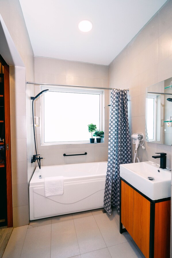 A bathroom with a bathtub, a sink, a mirror, and a window with a view of the outside. - Hotel Kimberly Tagaytay (Tagaytay)