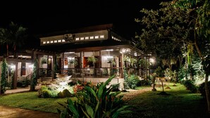 A well-lit, two-story building with a covered patio area, surrounded by lush greenery and plants. - Hotel Kimberly Tagaytay (Tagaytay)