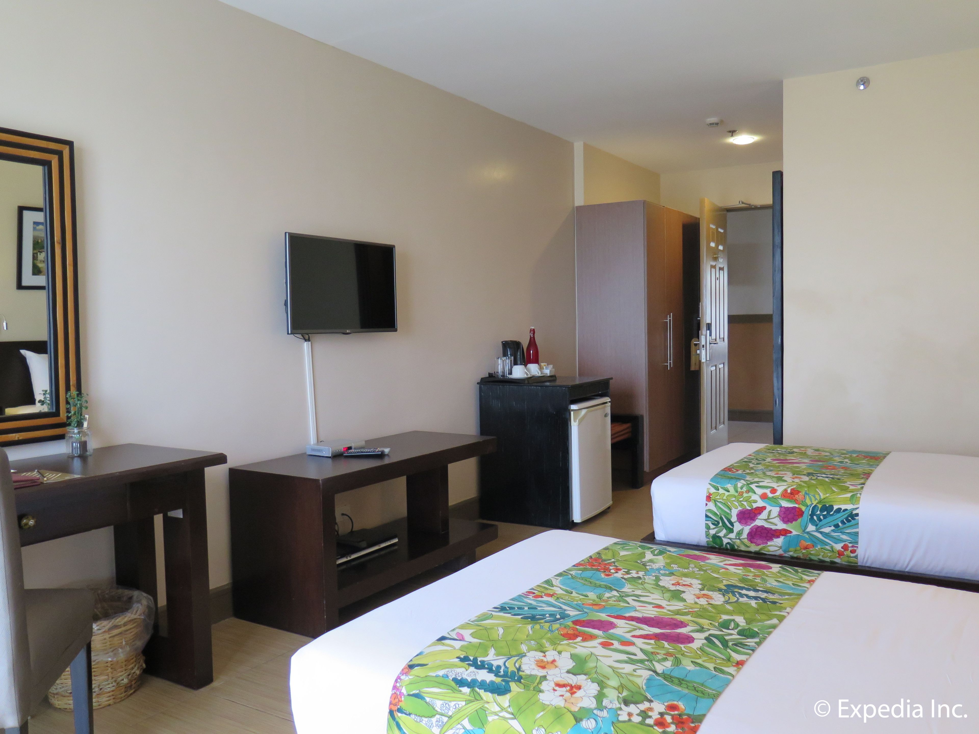 A hotel room with two beds, a desk, a television, a minibar, and a wardrobe.
