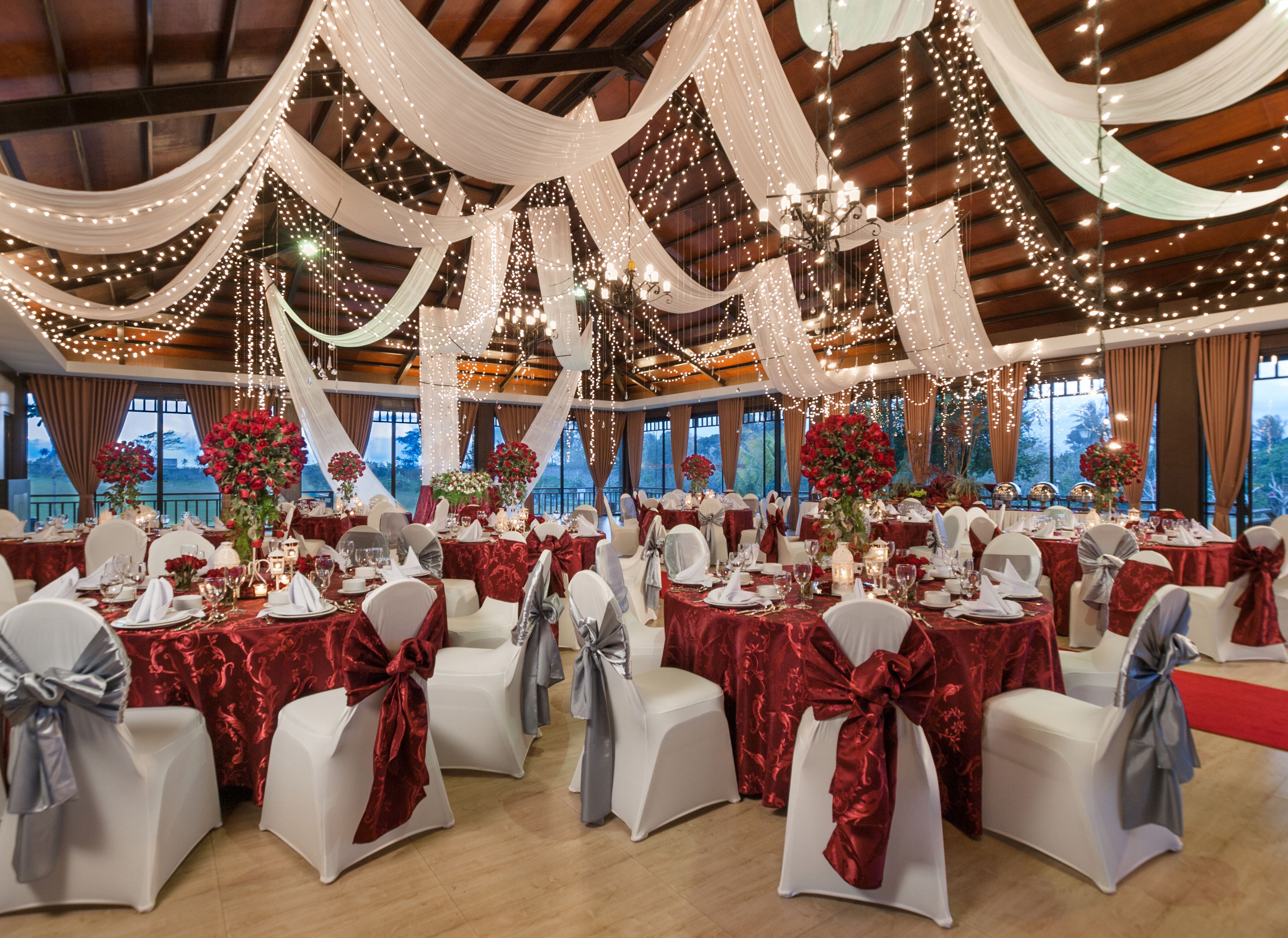 Un salón de banquetes con mesas dispuestas para un evento formal, cubiertas con tela blanca y luces de cuerda.