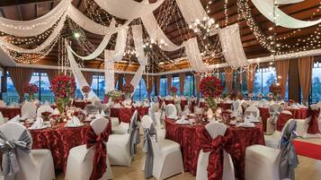 Un salón de banquetes con mesas dispuestas para un evento formal, cubiertas con tela blanca y luces de cuerda.
